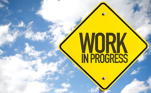 Yellow 'work in progress' sign against a blue sky with clouds